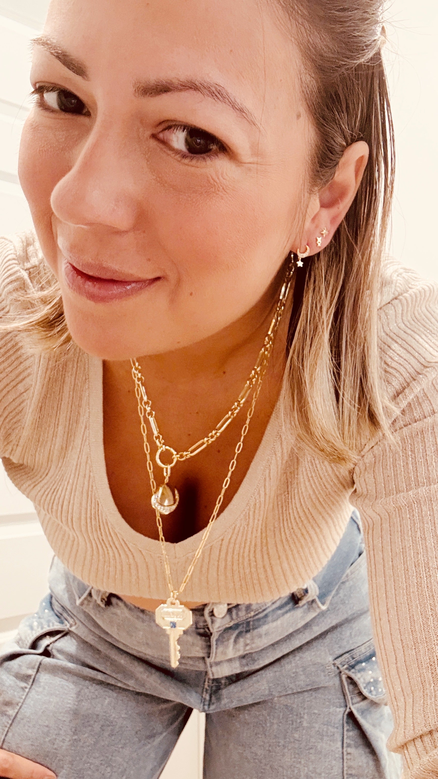 Woman wearing a gold necklace and earrings with a neutral background